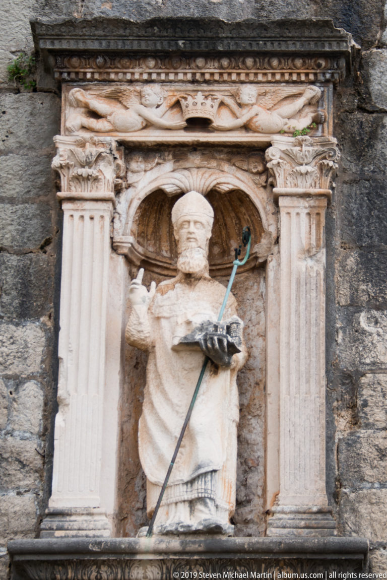 Stone statue of St Blaise holding a model of Dubrovnik in an architectural niche above Pile Gate.