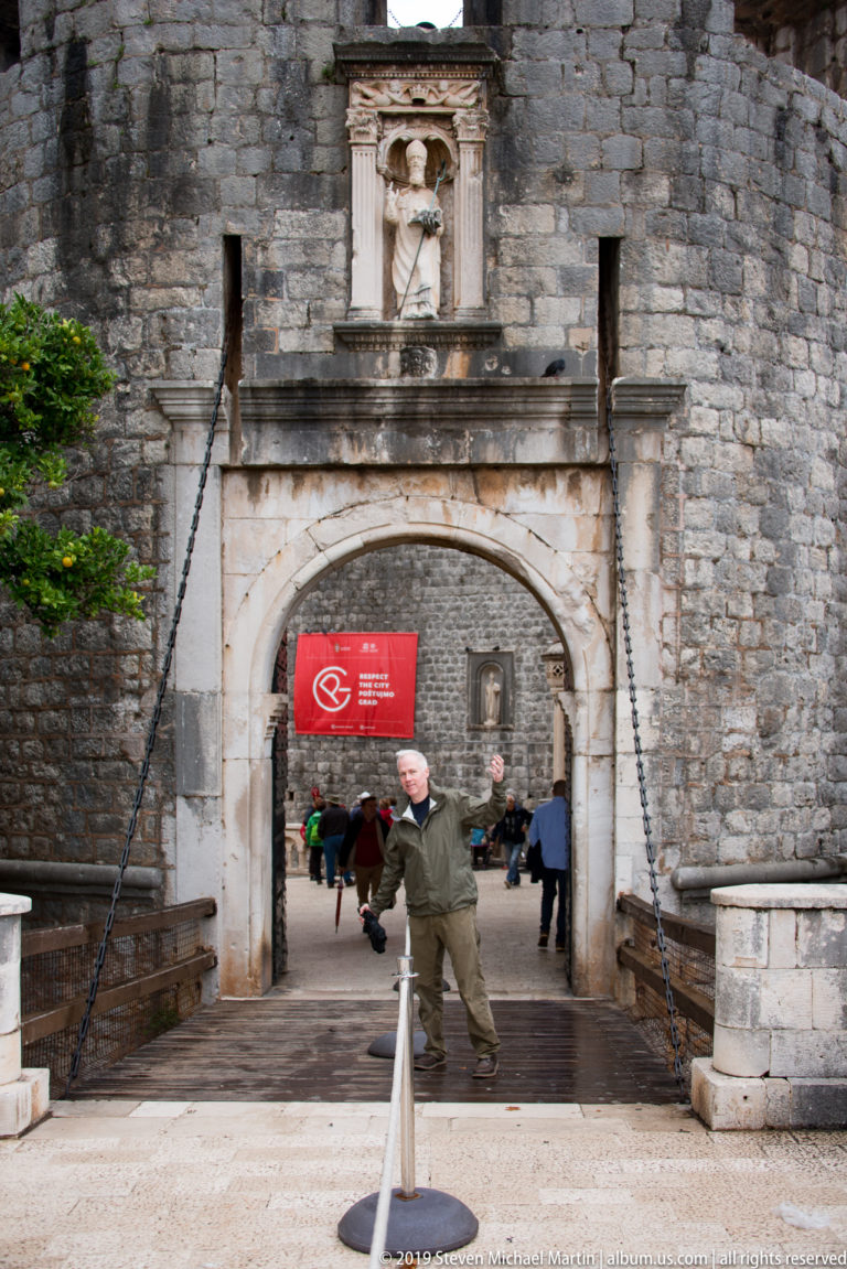 Pile Gate in Dubrovnik with broad stone arch, drawbridge chains, fortified masonry, and visitors passing into the Old Town.