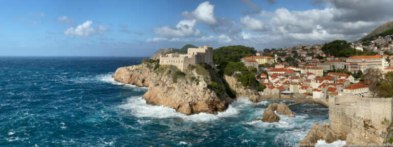 Stone fortress on a rocky promontory above rough blue sea and breaking waves.