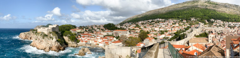 Dubrovnik red roofs and fortifications along rocky coast beneath a steep green hillside.