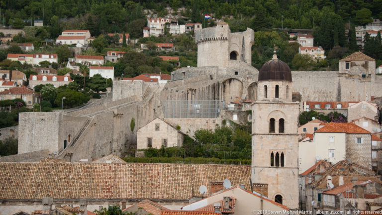 Bell tower and terracotta roofs in front of Dubrovnik’s massive crenellated city walls.
