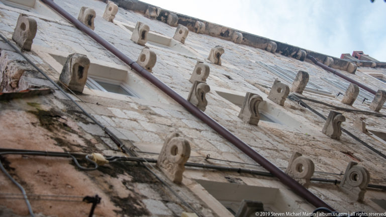 Oblique view up a stone façade lined with repeated projecting wall anchors.