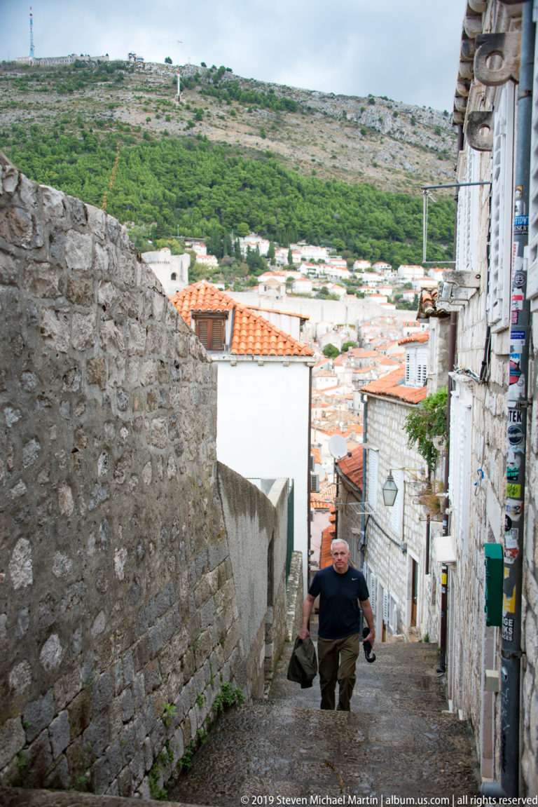 Man climbing a steep narrow stone street lined by high Dubrovnik masonry walls.