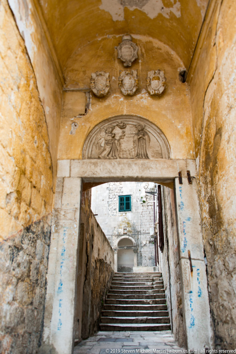 Weathered arched passage with carved relief above stone steps leading into Dubrovnik.