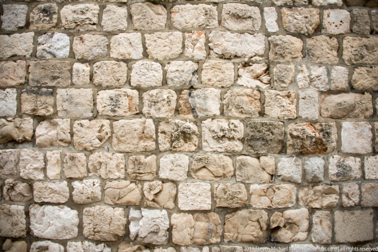 Close-up of irregular pale limestone blocks and mortar joints in a historic wall.