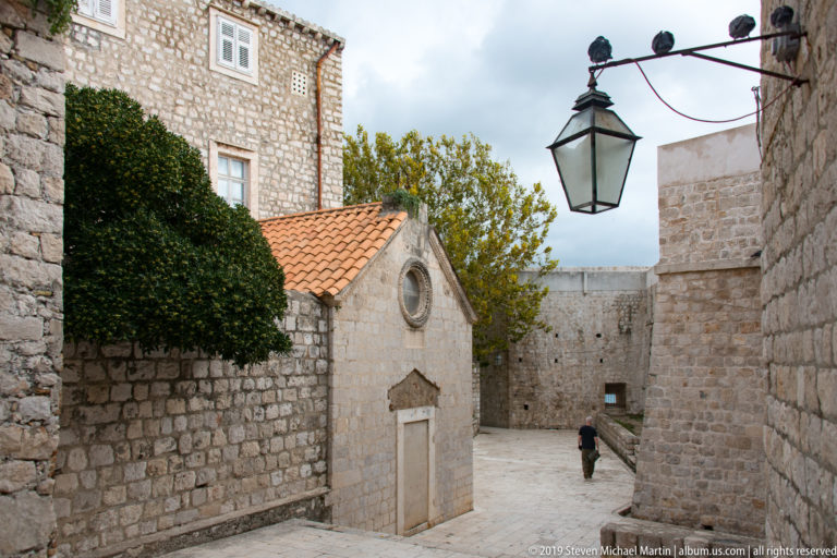 Narrow Dubrovnik lane with small chapel, stone walls, terracotta roof and hanging lantern.