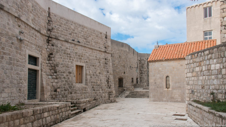 Open stone courtyard and stepped lane enclosed by thick historic masonry walls.