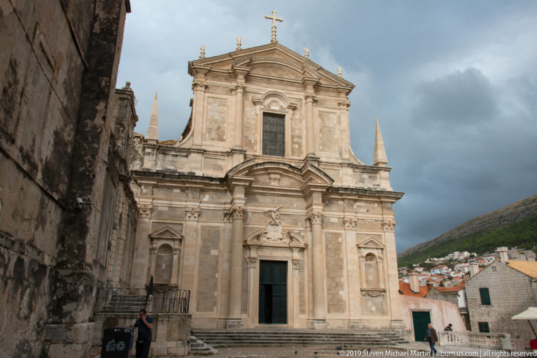 Baroque façade of Dubrovnik’s Jesuit Church of St Ignatius with pilasters, pediments, niches, and a cross above the entrance.