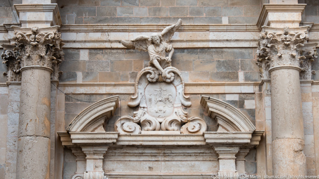 Stone doorway crowned by a Baroque cartouche, reclining figure, columns and layered cornices.