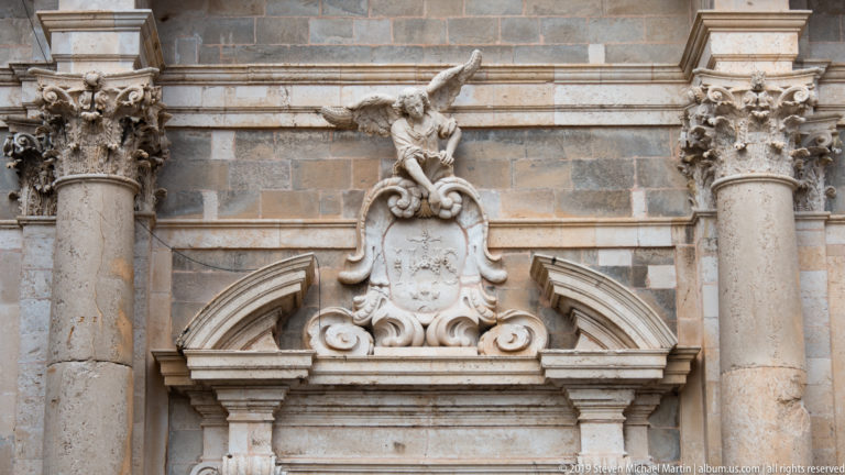 Stone doorway crowned by a Baroque cartouche, reclining figure, columns and layered cornices.