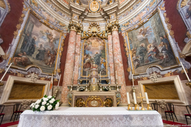 Ornate Baroque altar with red marble columns, gilded decoration and large religious paintings.