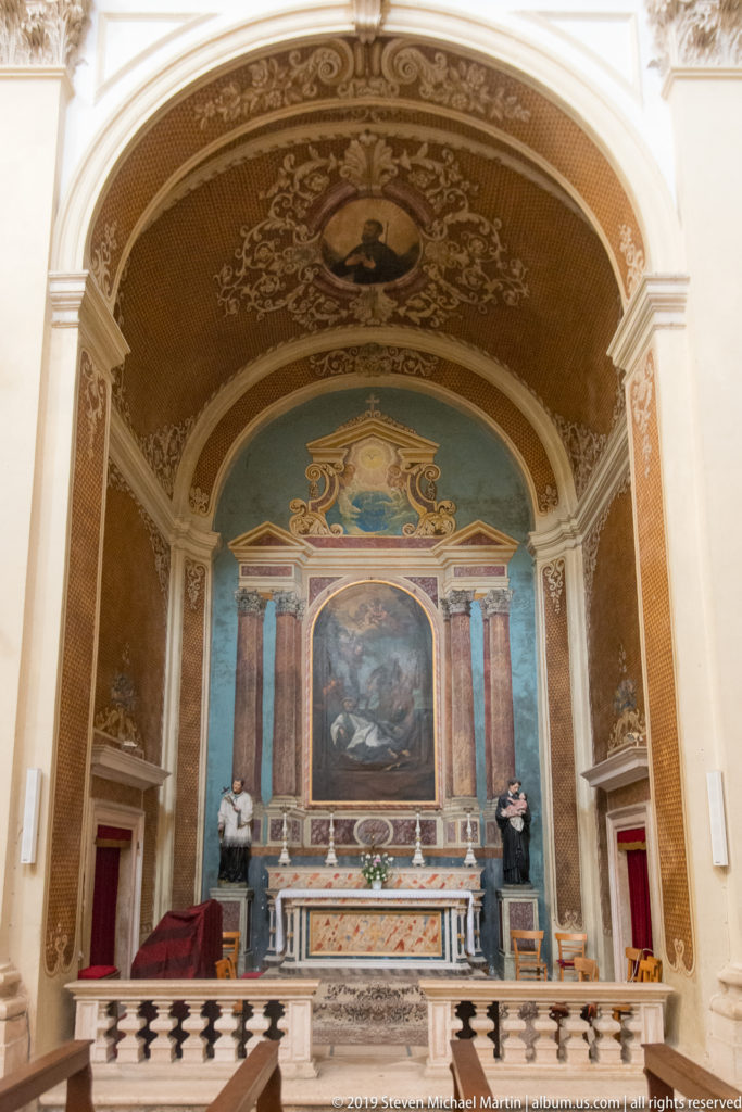 Marble chapel altar with central painting, sculpted figures and richly decorated barrel vault.