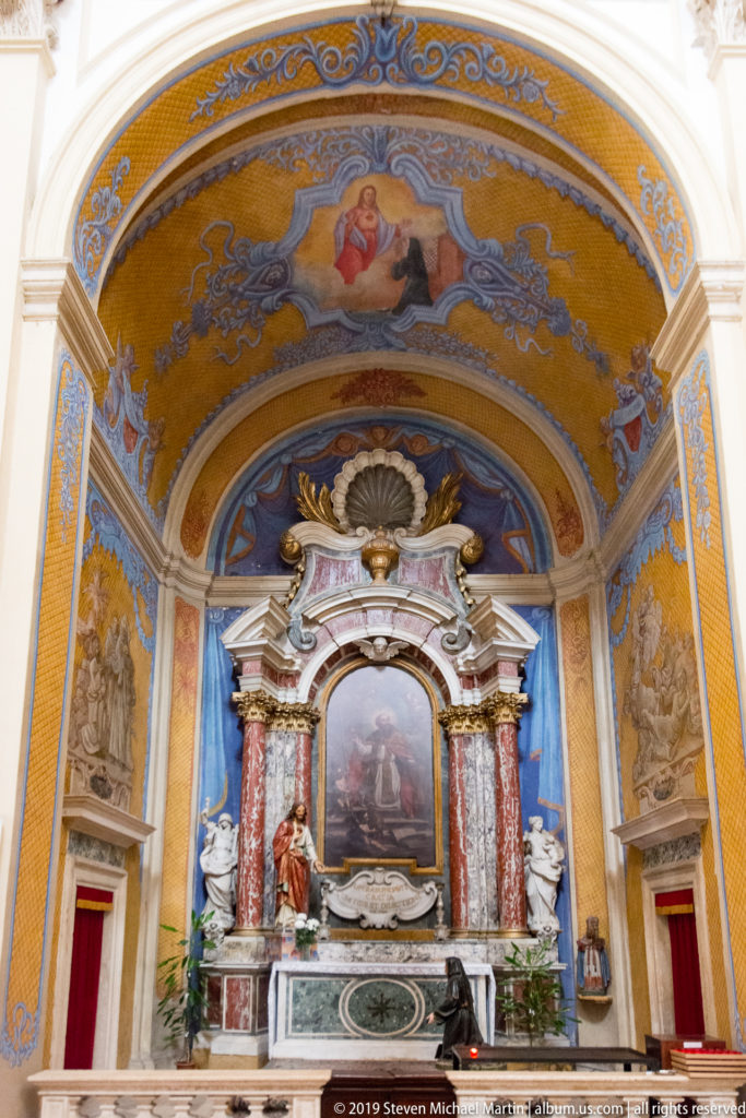 Baroque side altar with red marble columns, religious painting, sculpture and blue-and-gold painted vault.