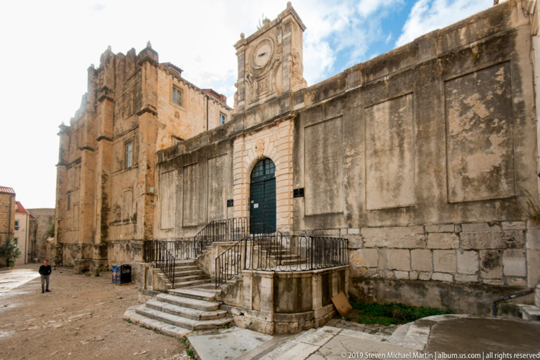 Weathered stone church façade with arched entrance, steps and adjoining tower in Dubrovnik.