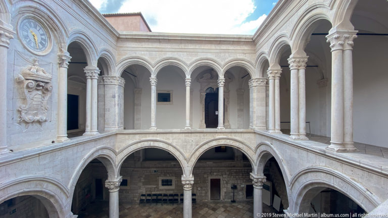 Symmetrical stone courtyard with two levels of rounded arches, carved columns and open sky.