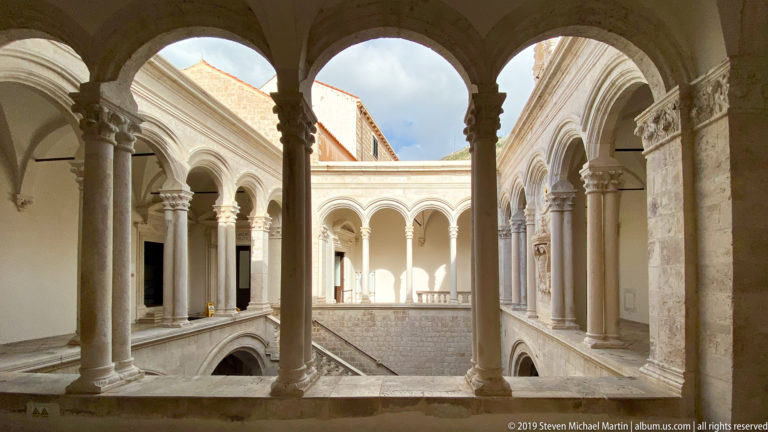 Upper stone arcade with slender columns and rounded arches surrounding an open courtyard.