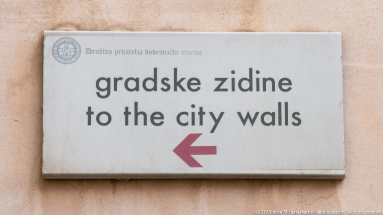 White bilingual sign reading “gradske zidine / to the city walls” with a red left arrow.