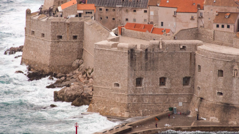 Massive stone fortress on Dubrovnik’s waterfront with waves breaking below and Old Town buildings behind.