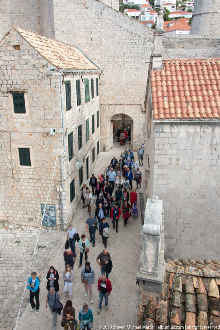 Crowd of visitors in a stone courtyard and passage beneath Dubrovnik’s walls.