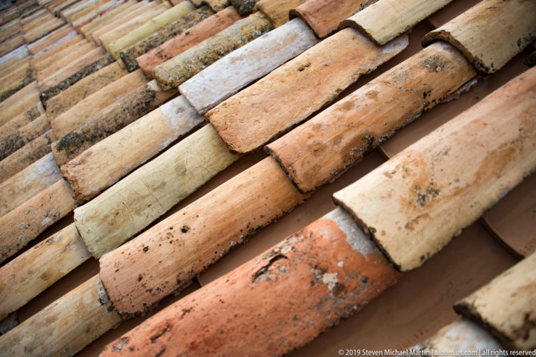 Close-up of overlapping weathered clay roof tiles in cream, ocher and orange tones.
