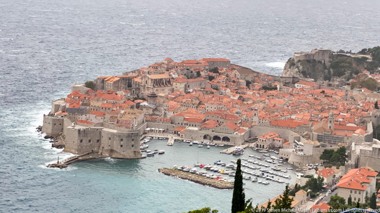 Telephoto view of Dubrovnik’s red roofs and massive western waterfront fortifications beside turquoise water.