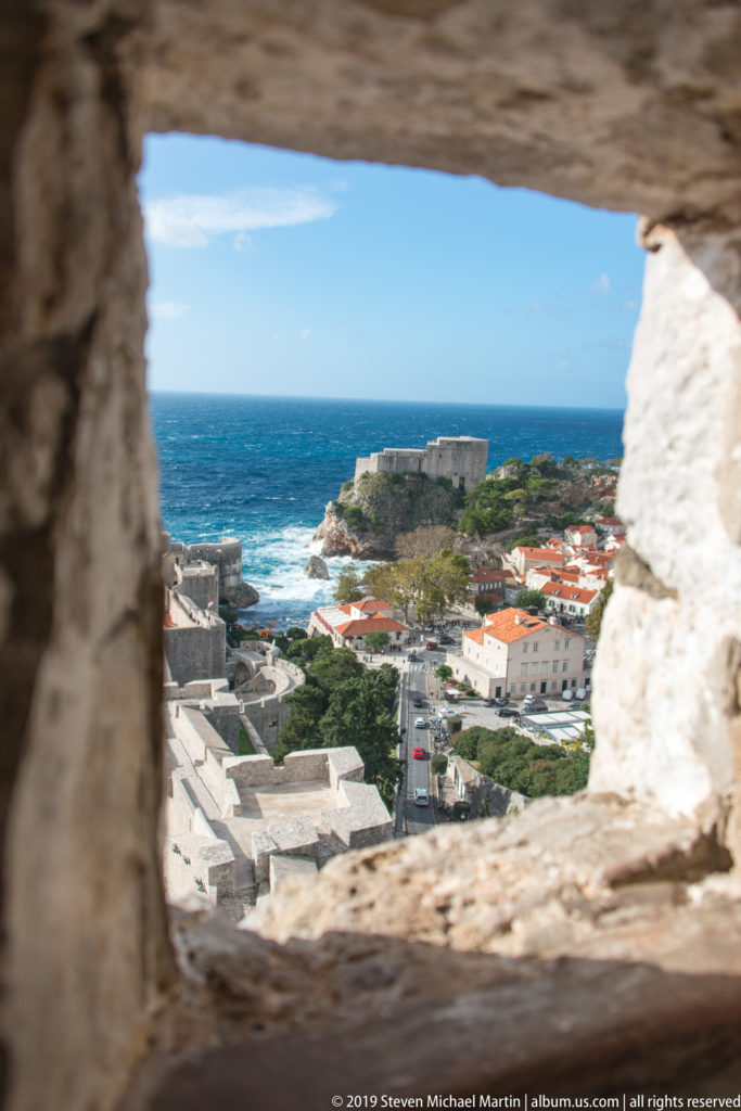 Fort Lovrijenac and the Adriatic are seen through a thick rectangular opening in Dubrovnik’s rough stone fortifications.