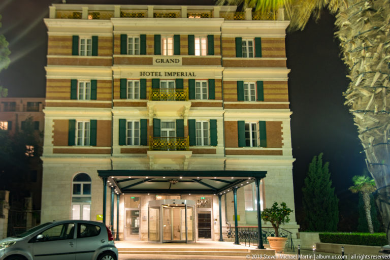 Illuminated Grand Hotel Imperial façade with green shutters, balconies, striped masonry, and entrance canopy at night.