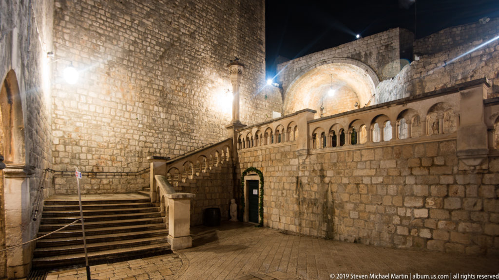 Stone staircase and balustraded ramp enclosed by heavy masonry within Dubrovnik’s western gate complex at night.