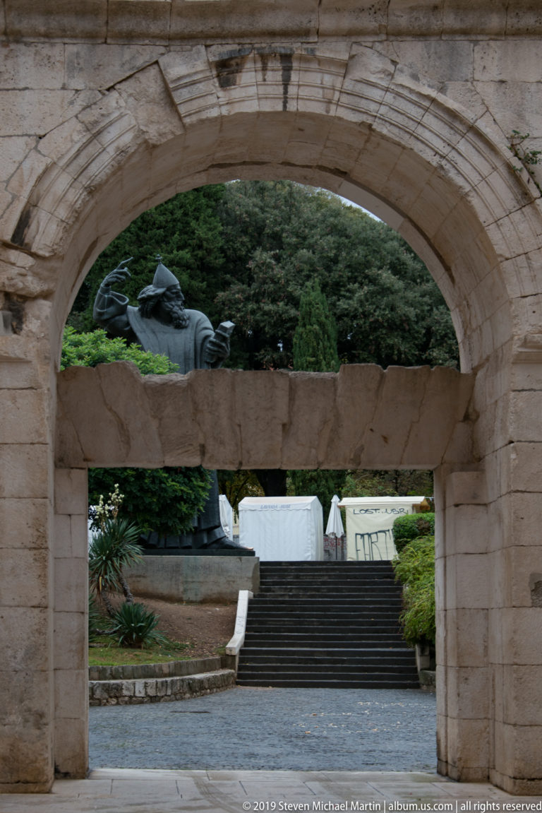 Broad stone arch and lintel framing steps with the Gregory of Nin statue visible beyond.