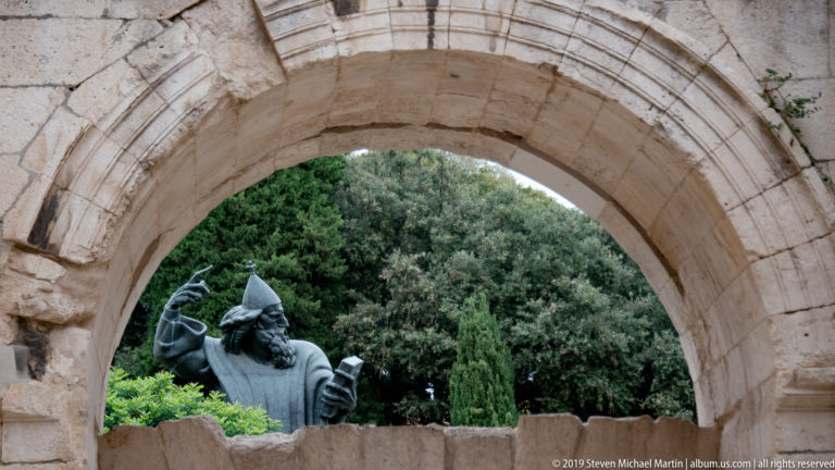 Gregory of Nin statue seen through a large pale stone arch with trees behind.