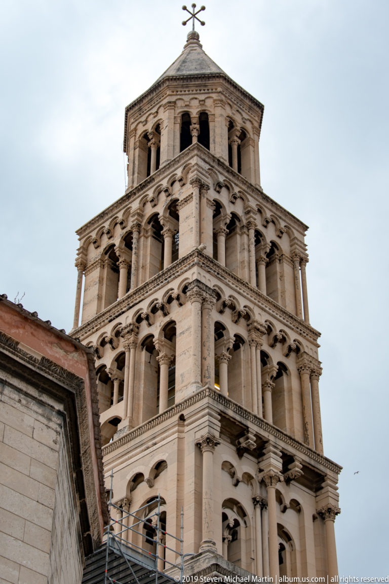 Tall pale stone bell tower with multiple arcaded levels rising above nearby roofs.