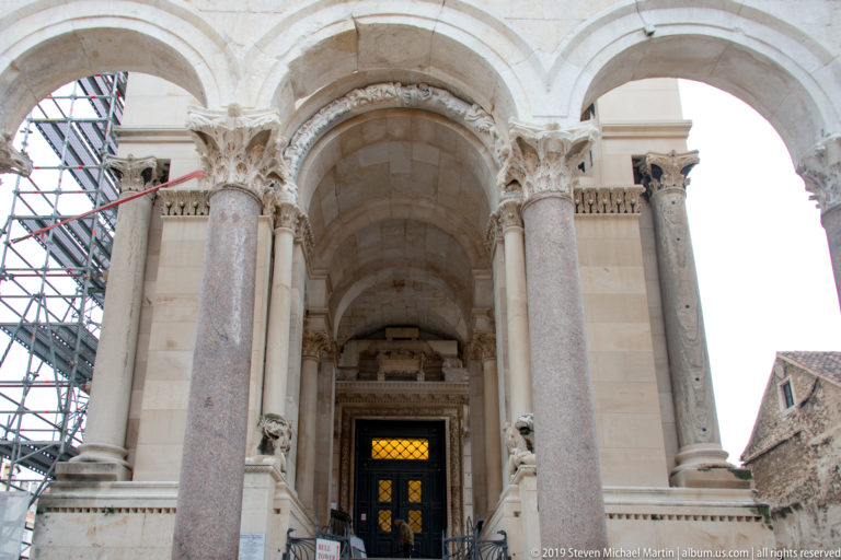 Upward view of the Cathedral of Saint Domnius entrance with tall columns, carved capitals, arches, and a recessed doorway.