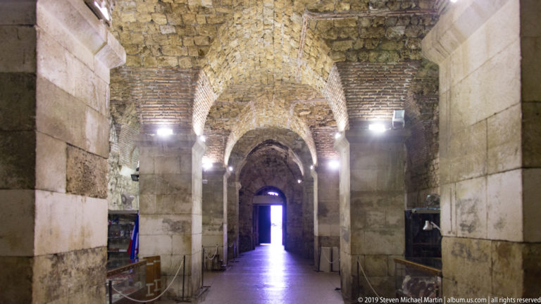 Long vaulted stone chamber with massive piers and a bright doorway in the substructures of Diocletian’s Palace.