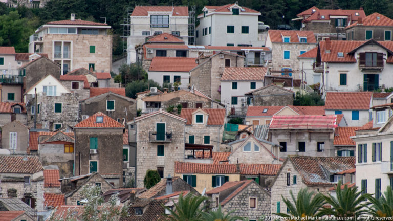 Dense hillside neighborhood of stone houses, red tile roofs, shutters, and balconies in Split.