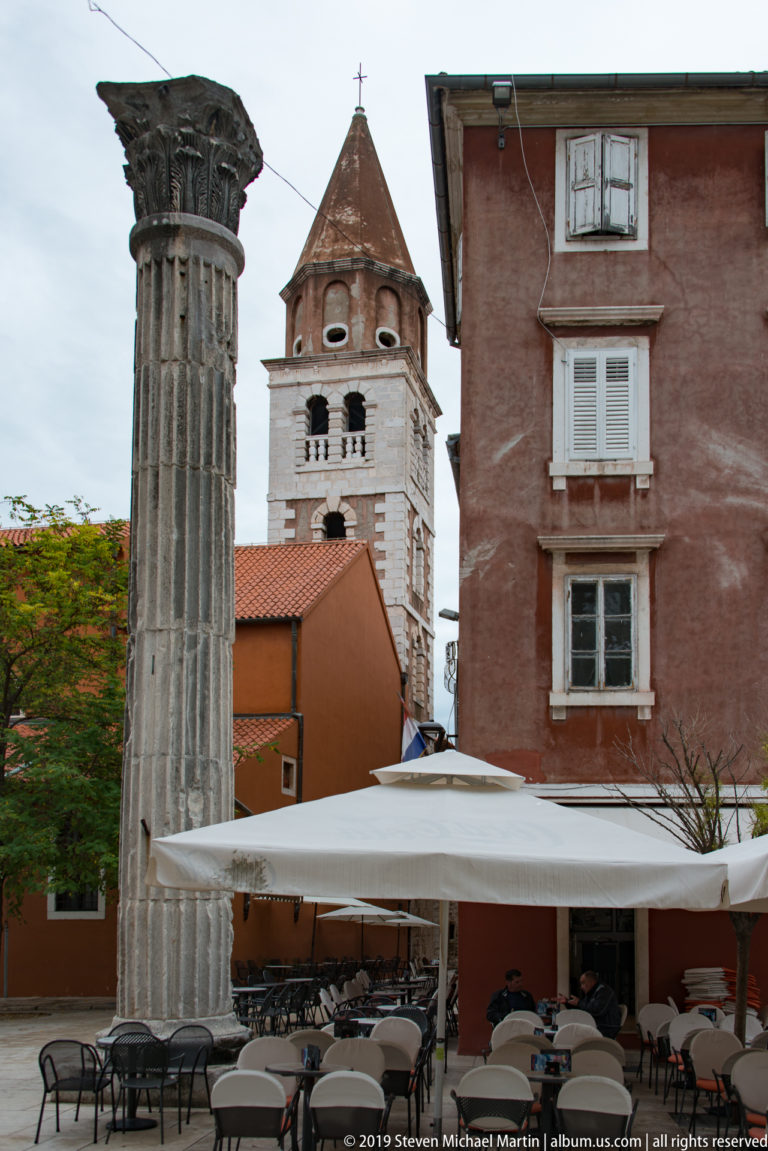Ancient fluted stone column with carved capital standing among cafés and historic buildings in central Zadar.