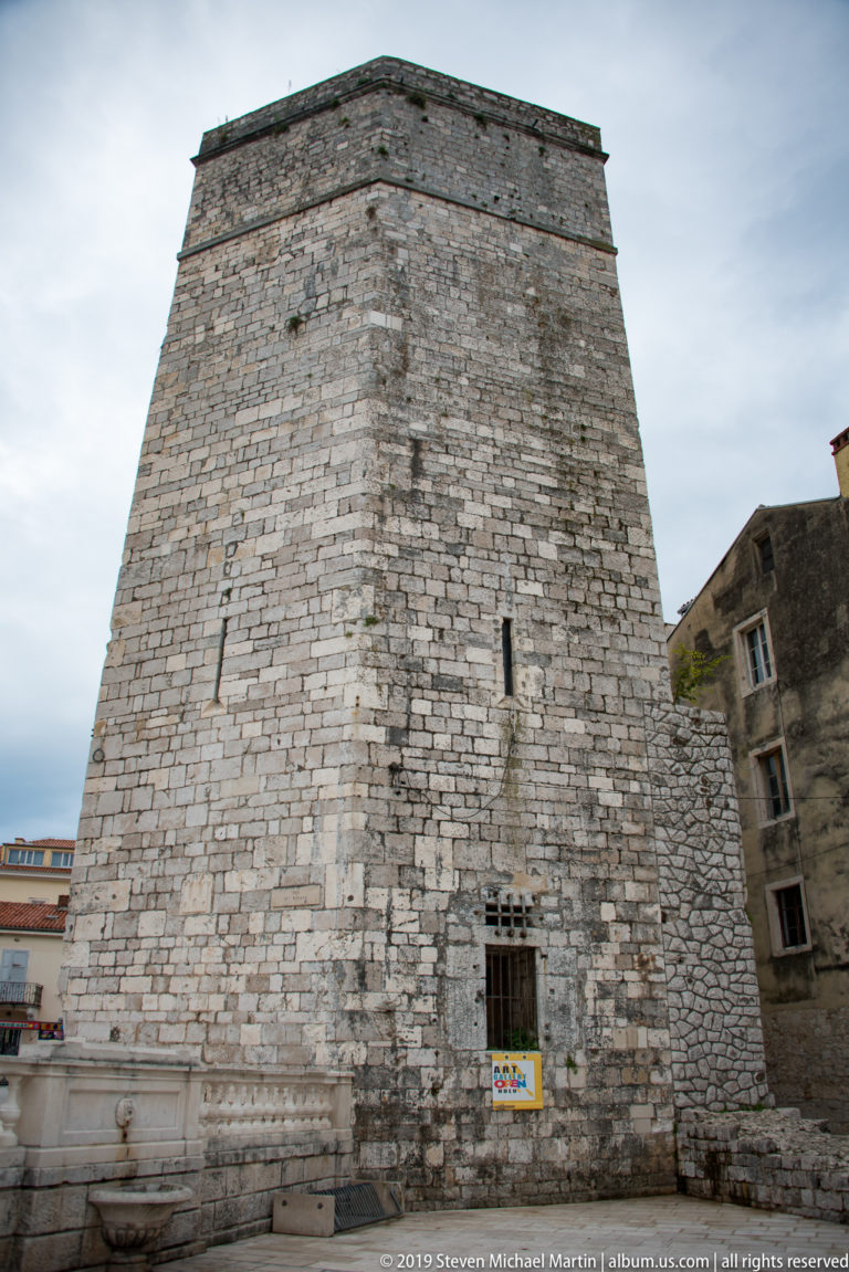 Oblique view of the massive stone Captain’s Tower with battered walls, slit windows, and adjacent fortifications.
