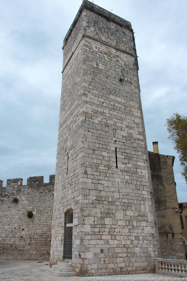 Massive tapering stone Captain’s Tower with narrow slit opening beside the fortification wall in Zadar.