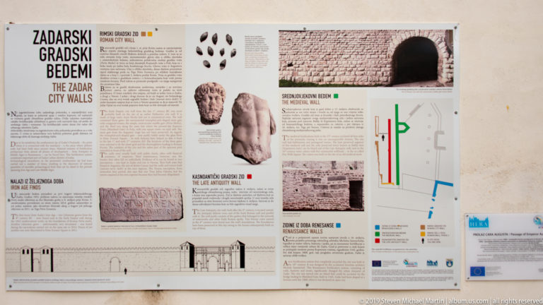 Large outdoor heritage panel with maps, wall photographs, archaeological finds, and bilingual text about Zadar city walls.