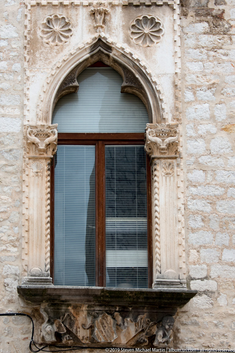 Pointed Gothic window with twisted side columns, carved capitals, cusped arch, and small rosette above.
