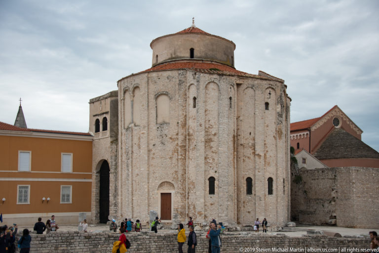 Rounded exterior of the Church of St. Donatus with tall blind arches, narrow openings, and red-tiled roof.