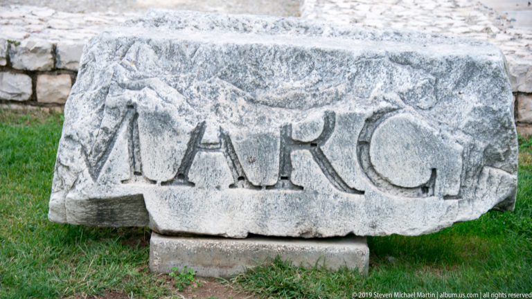 Broken Roman stone block with large deeply carved capital letters, including the surviving sequence MARC.