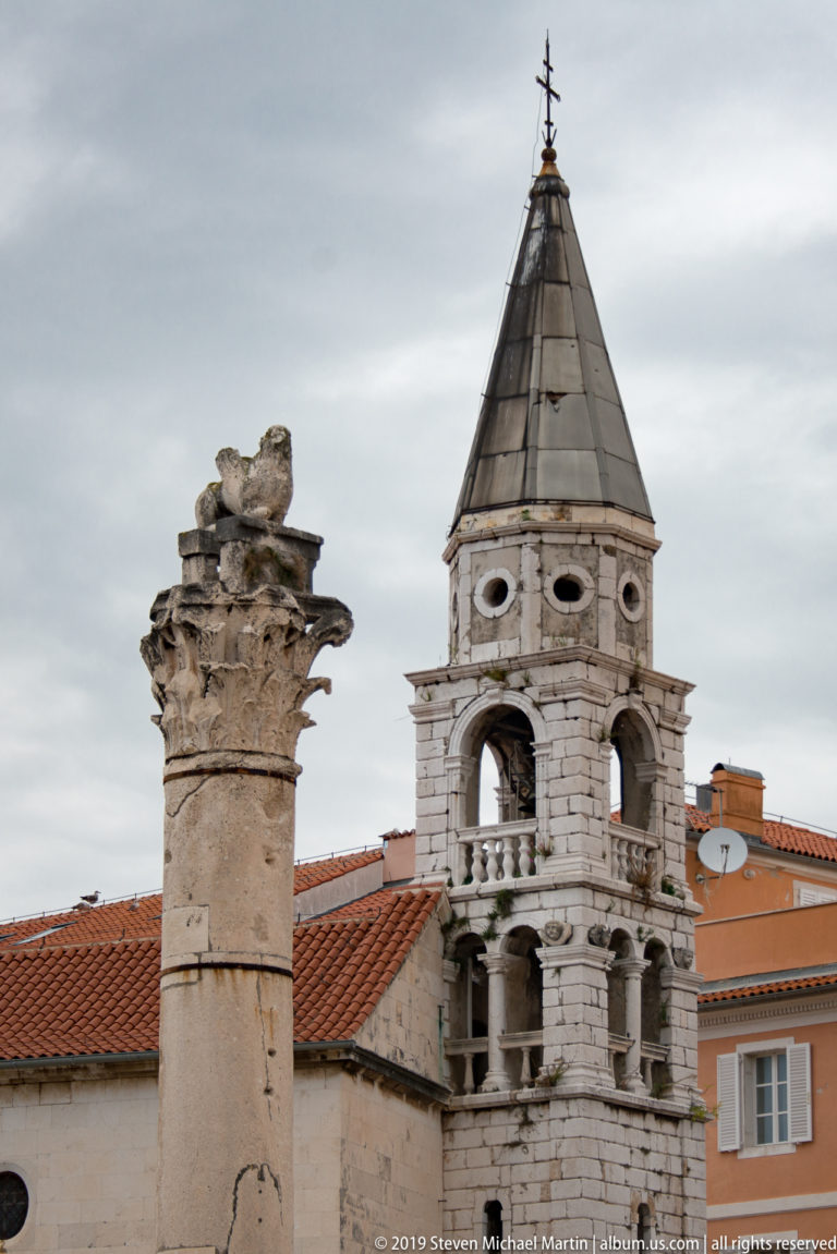 Ancient carved column in the foreground with the arcaded bell tower of St. Mary’s Church behind.