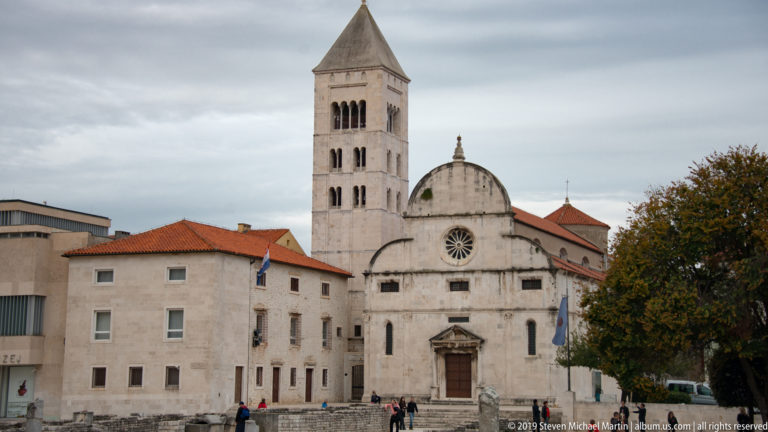 Church of St. Mary in Zadar with pale façade, rose window, dome, and tall square bell tower at left.