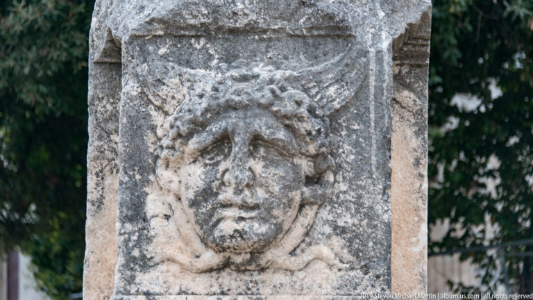 Weathered stone relief of an idealized face with large eyes and curling hair on an ancient block.