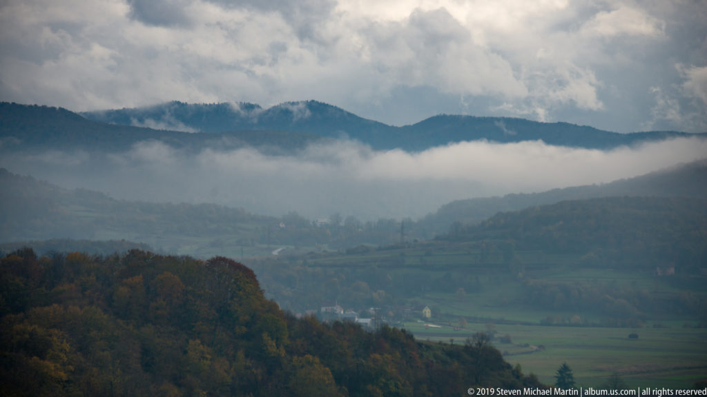 Layered wooded hills and green valley fields under low cloud and mist in the inland landscape near Zadar.