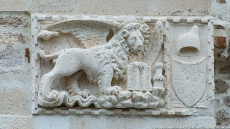 Worn stone relief of the winged Lion of Saint Mark with an open book beneath its forepaw.