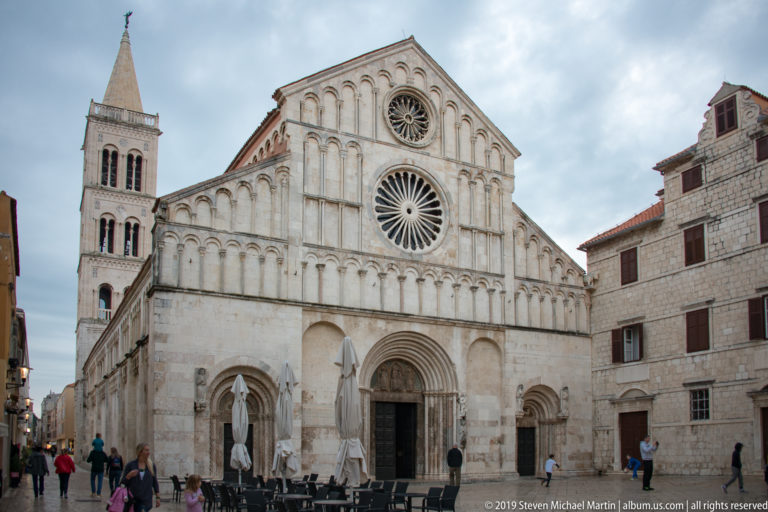 West façade of St. Anastasia Cathedral with two rose windows, blind arcades, Romanesque portal, and bell tower at left.