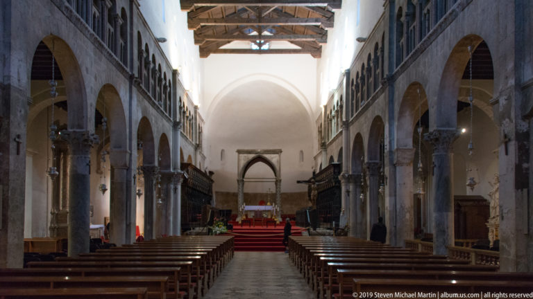 St. Anastasia Cathedral nave with stone arcades, timber roof, wooden pews, choir stalls, and raised sanctuary.