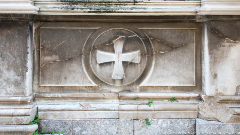 White stone cross in a circular medallion carved into a weathered masonry wall.