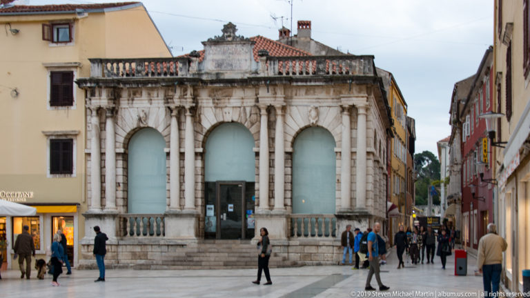 Zadar City Loggia with three tall arches, paired columns, balustrade, inscription panel, and pedestrians in front.